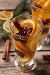 Delicious mulled white wine with slices of orange and spices in glass cup on wooden table, closeup