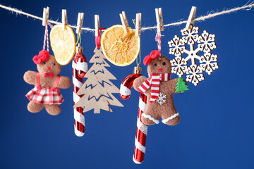 Different Christmas decor hanging on string against blue background, closeup. New Year greeting card