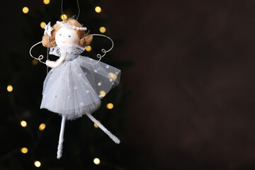 Fototapeta premium Christmas decor. Fairy doll hanging on black background with blurred lights, closeup. Space for text