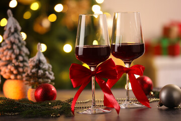 Glasses of red wine and Christmas decor on wooden table against background with blurred lights