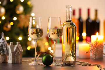 Glasses of white wine, bottle and Christmas decor on wooden table against background with blurred lights