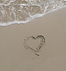 Heart shaped painting on a light brown sandy beach with a wave beautiful love concept
