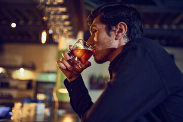 Man enjoying classic drink at dimly lit bar counter. Concept of evening unwind, bar culture, beverage tasting sessions, and relaxed after-work atmosphere.