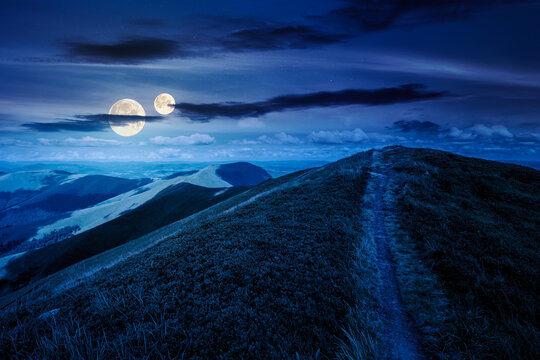 path to the mountain top at night. beautiful summer scenery with dynamic clouds on a dark sky in full moon light. scenic landscape with rolling hills. background for fake news or conspiracy concepts