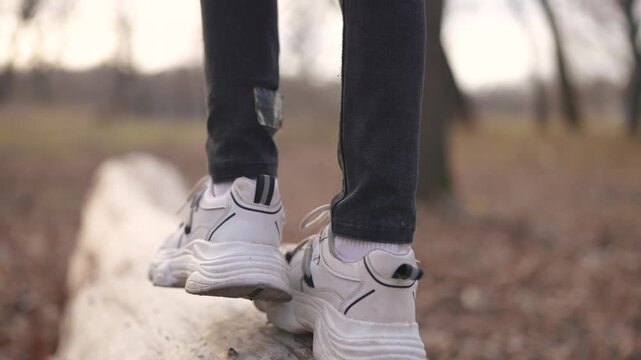boy play in a forest park. A close-up of a child's feet walking along a log of a fallen tree. happy family lifestyle child dream concept. girl child in sneakers walks on a fallen tree in a park