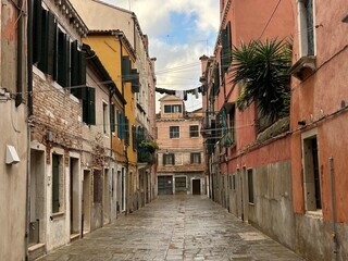 A narrow Venetian street leading to an older building, framed by tall, colorful, and weathered facades.Laundry hangs across the street in the distance, adding a touch of authentic, everyday life.