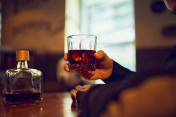 Hand holding whiskey glass beside bottle on wooden table. Concept of alcohol product placement, tasting visuals, bar lifestyle campaigns, and premium spirit advertising assets.