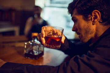 Man examining whiskey glass with bottle on table. Concept of tasting rituals, premium spirit positioning, alcohol storytelling, and lifestyle imagery for crafted drink marketing.