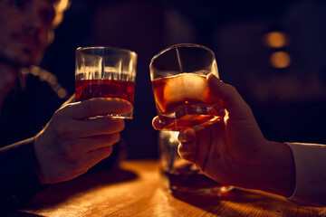 Two hands raising whiskey glasses for evening toast. Concept of shared bar rituals, crafted spirit appreciation, premium alcohol marketing materials, and warm night atmosphere.
