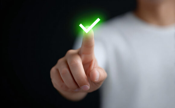 Hand touching glowing green check mark icon indicating success and correct decision with confident and positive emotion on dark background