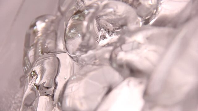 Close-up horizontal video of melted ice cubes floating on water as the camera gently hovers above them, capturing soft reflections, shifting light, and subtle organic movements.