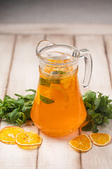 Refreshing citrus drink with mint, orange slices and ice served in a glass pitcher on rustic wooden table