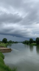 Fototapeta premium Wide River Landscape with Moody Sky. Serene River Flow Under Stormy Clouds. Tranquil River in Natural Setting.