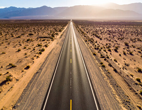 Endless straight desert highway stretching towards distant mountains at sunset road
