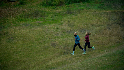 Two runners moving through wide grassy hillside trail. Concept of steady cardio, daily routine, outdoor balance, wellness habits, relaxed pace, nature-focused lifestyle.