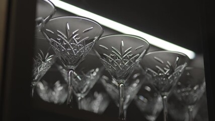 Crystal martini glasses stand in reflective row showing abstract patterns. Polished shapes create elegant sparkling presentation on shelf - Powered by Adobe
