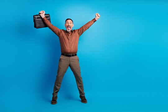 Businessman celebrates success with raised briefcase against blue studio background