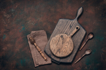 Various wooden kitchen utensils on dark brown grunge background, wooden cutting boards, wooden spoons, honey dipper, linen napkin, top view, flat lay