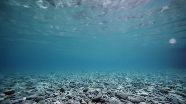 Underwater view of clear blue sea with rocky bottom and sunlight.