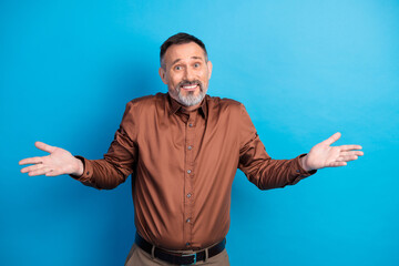 Confident mature businessman with open arms smiling at camera in a brown shirt against a blue...