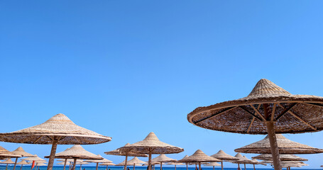 Row of woven straw beach sun parasols with vivid blue sky ideal for travel advertising and resort posters