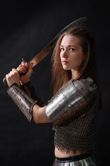 Obraz premium Portrait of a young woman, fantasy warrior in armor with a sword in her hands isolated on a dark background.
