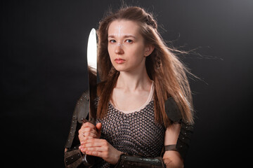Obraz premium Portrait of a young woman, fantasy warrior in armor with a sword in her hands isolated on a dark background.