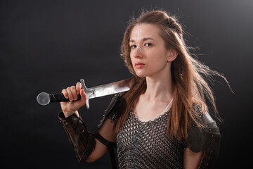 Obraz premium Portrait of a young woman, fantasy warrior in armor with a sword in her hands isolated on a dark background.