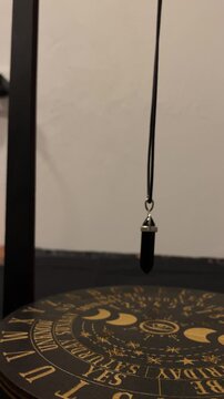 Pendulum over a spirit board on a wooden table with candles esoteric occult divination ritual, mystical altar, magical tools, fortune telling setup