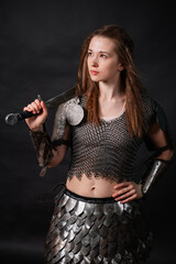 Obraz premium Portrait of a young woman, fantasy warrior in armor with a sword in her hands isolated on a dark background.