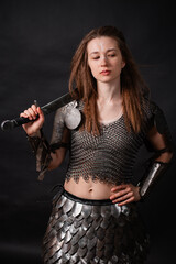 Obraz premium Portrait of a young woman, fantasy warrior in armor with a sword in her hands isolated on a dark background.