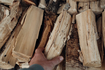 Close-up of a man's hand taking a cut and split logs from a neatly stacked pile of firewood, perfect for a cozy fireplace or outdoor fire pit