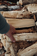 Close-up of a man's hand taking a cut and split logs from a neatly stacked pile of firewood, perfect for a cozy fireplace or outdoor fire pit