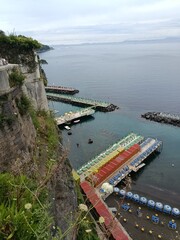 Sorrento, Italy &mdash; Overlooking beach platforms and calm bay waters beneath steep cliffs, this scene blends vivid seaside colors with peaceful coastal relaxation, evoking Mediterranean summer calm.