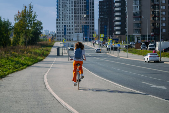 Woman rides a city bicycle along a dedicated bike lane, moving away from camera with urban buildings and traffic in background, symbolizing eco-friendly commuting and fitness