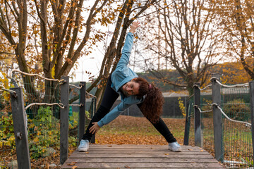 Woman performing a yoga pose on a wooden bridge, enjoying active wellness outdoors