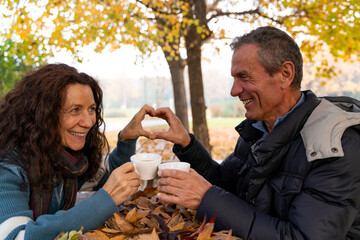 Senior couple making a heart gesture while enjoying coffee among autumn leaves in a park