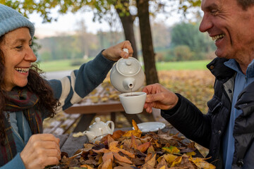 Happy senior couple sharing tea during an autumn picnic in the park
