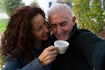 Happy senior couple smiling, drinking coffee, and taking a selfie in a park