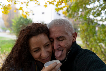 Mature couple showing affection, man sticking out tongue while woman smiles holding a cup