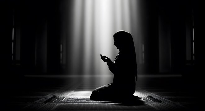 Silhouette of Muslim Woman Praying on a Prayer Mat Under Light Beams