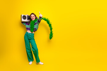 Young woman dancing with a boombox against a bright yellow background wearing a striped sweater and green pants for a lively fashion lifestyle image