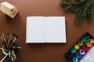 High angle view of children’s creative Christmas decorations with blank canvas surrounded by art materials. Colourful creative background for Christmas and Happy New Year, flat lay with copy space.