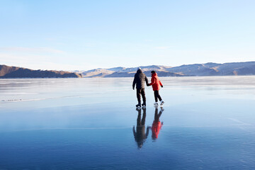 A couple is skating on the frozen Lake Baikal. Transparent ice.