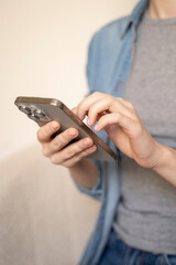 Vertical сlose up of female's hands holding mobile phone, scrolling her social media, messaging, browsing online content, and internet shopping indoors while sitting on a sofa at home.