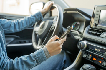 Close up of distracted woman's hands using mobile phone while driving a car, texting and scrolling, an illegal, unsafe and dangerous behavior on a road, that can cause a tragic accident.