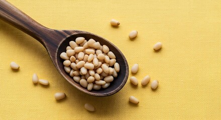 Wooden spoon holding pine nuts scattered on a yellow textured surface.