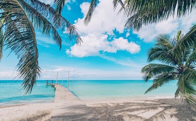 A beautiful tropical landscape featuring a pier extending into the turquoise ocean. Palm leaves...