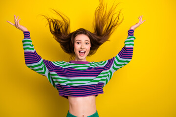 Young woman in colorful striped sweater leaps with joy against a bright yellow background