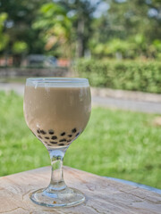 Bubble milk tea in a clear glass on a wooden plate